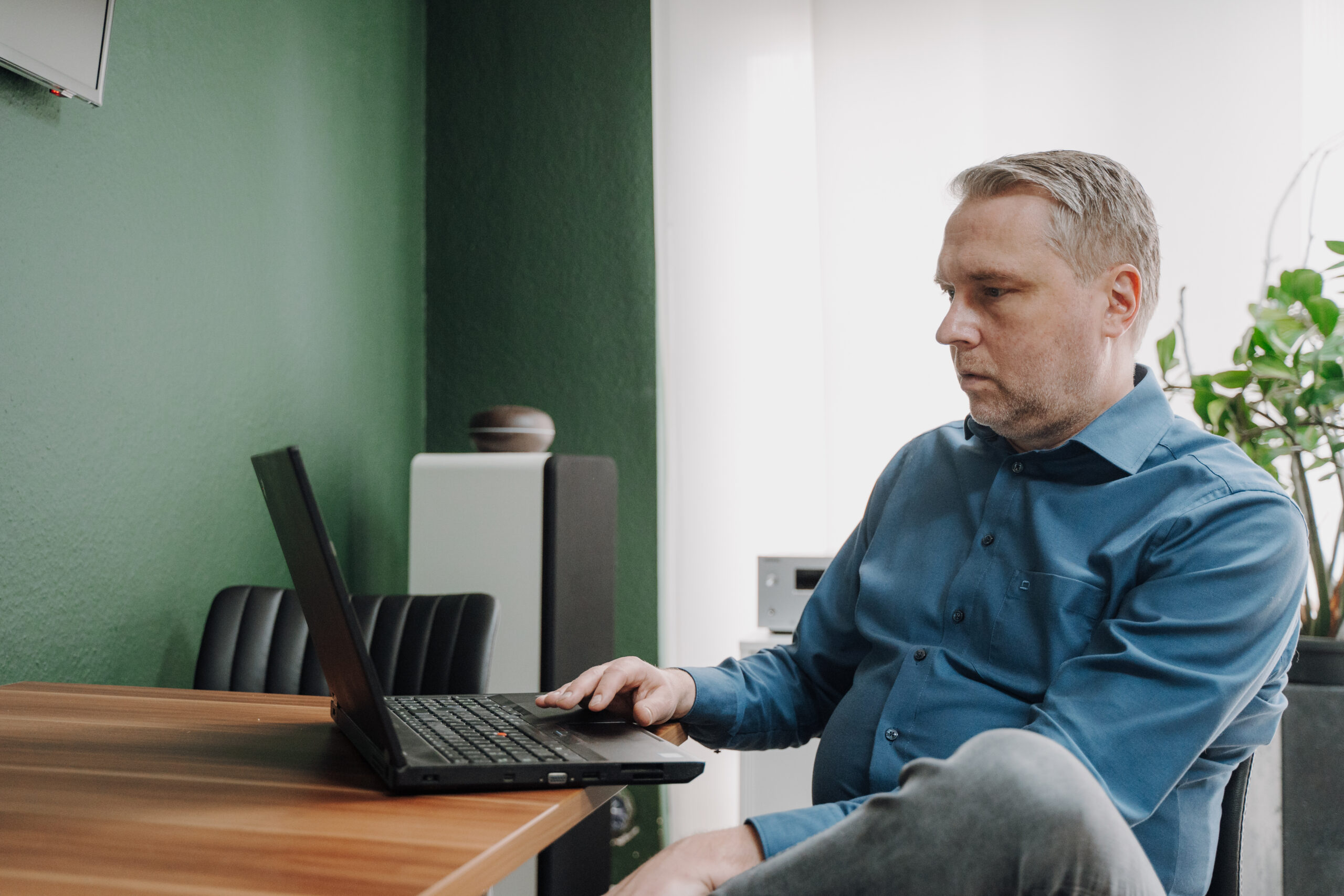 mann sitzt an einem laptop in einem buero mit gruenen waenden